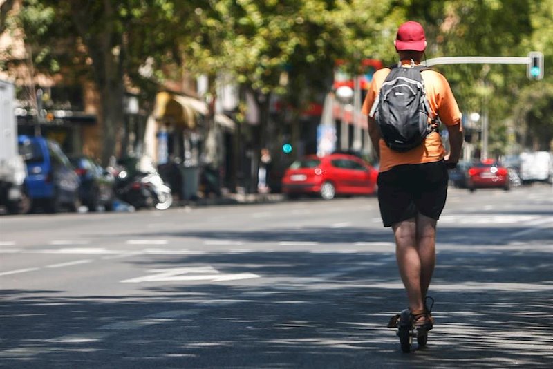 ep un hombre cicula en un patinete por una calle de madrid junto a diferentes coches