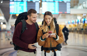 ep pareja en el aeropuerto con un telefono que muestra un billete y una aplicacion de viajes ambos