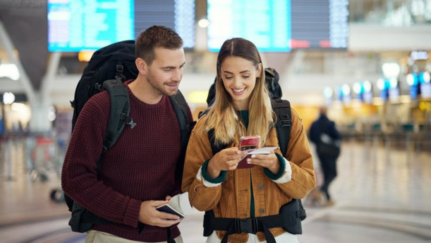 ep pareja en el aeropuerto con un telefono que muestra un billete y una aplicacion de viajes ambos